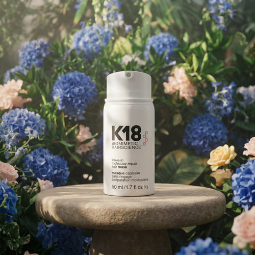K18 Leave-In Molecular Repair Hair Mask 50ml bottle on pedestal with blue flowers in garden setting