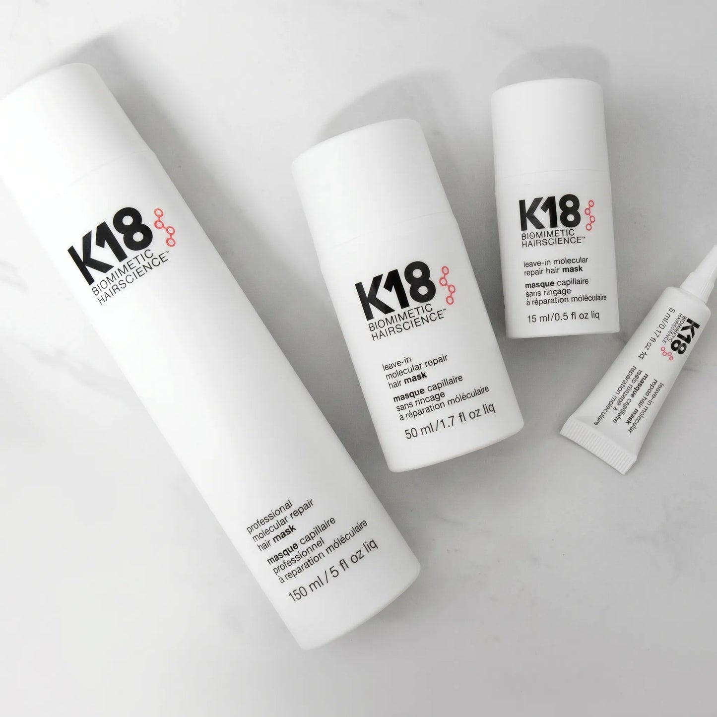 K18 Molecular Repair Hair Mask product set with 150ml, 50ml, 15ml and tube on marble background