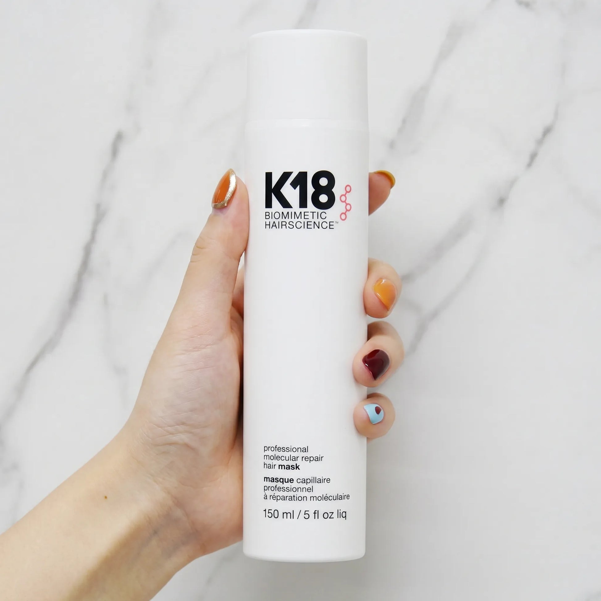 Hand holding K18 Professional Molecular Repair Hair Mask 150ml bottle against marble background