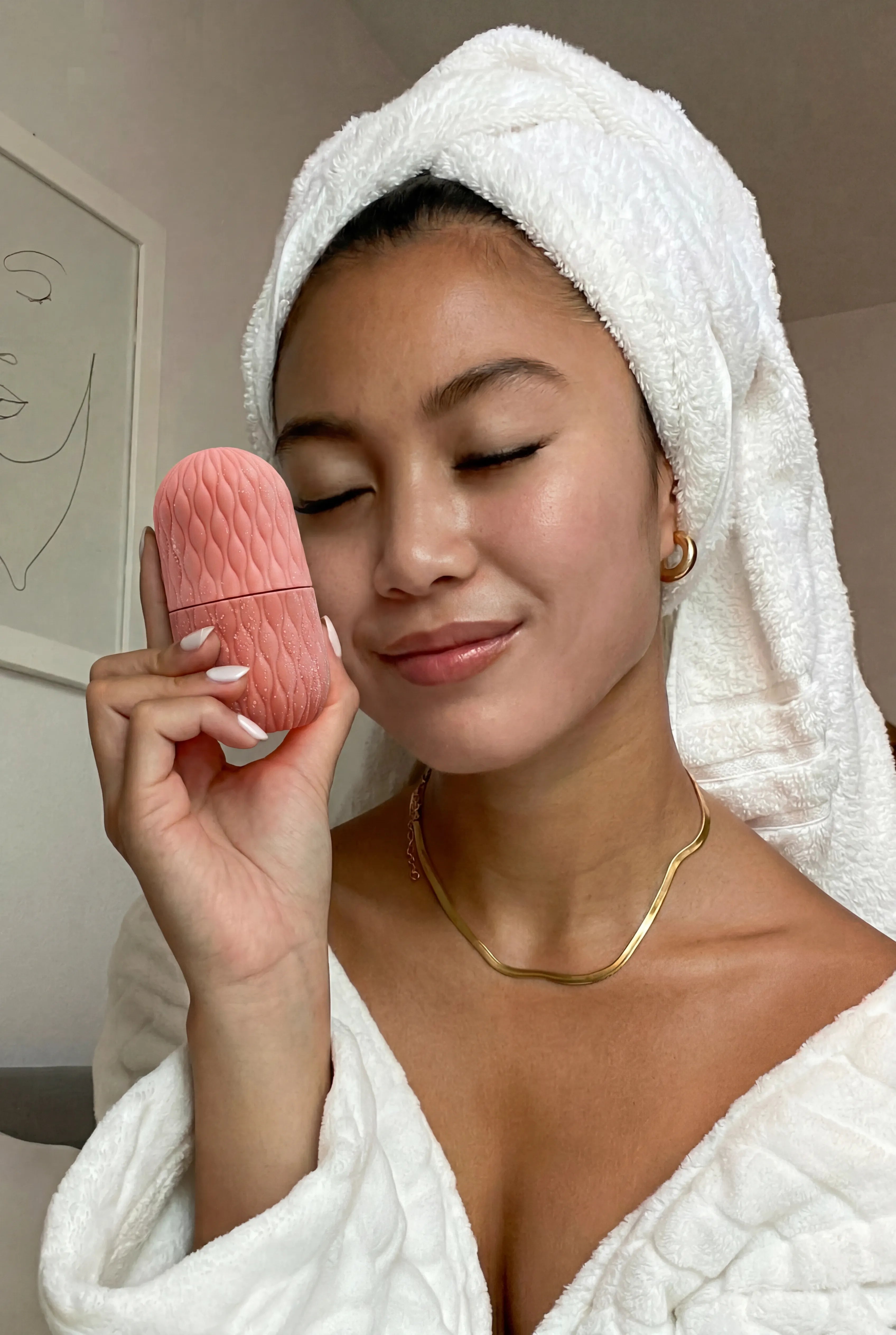 Woman holding pink Velivor Glace Ice Roller during skincare routine with towel wrap